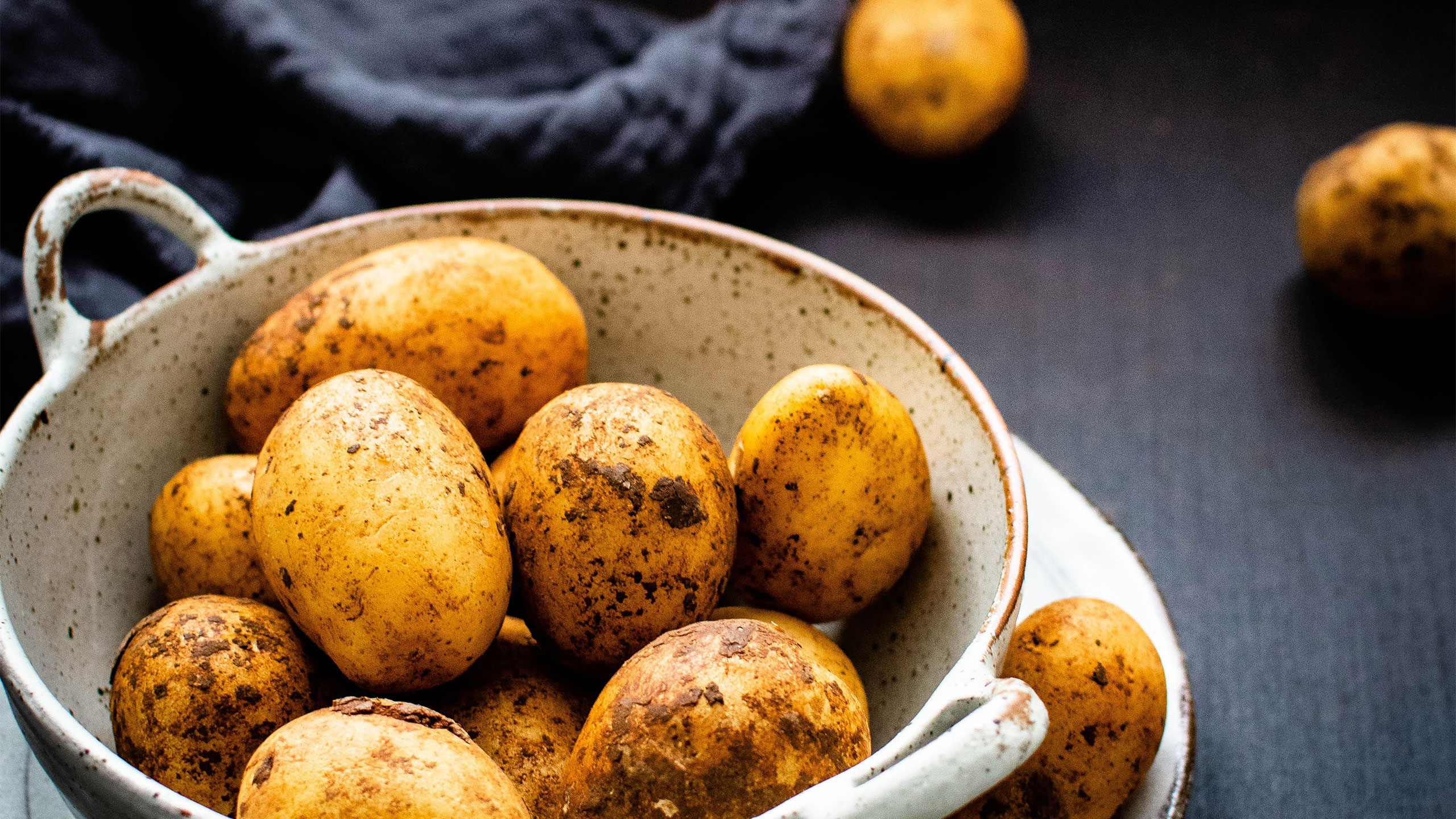 A bowl of potatoes, some still covered in dirt