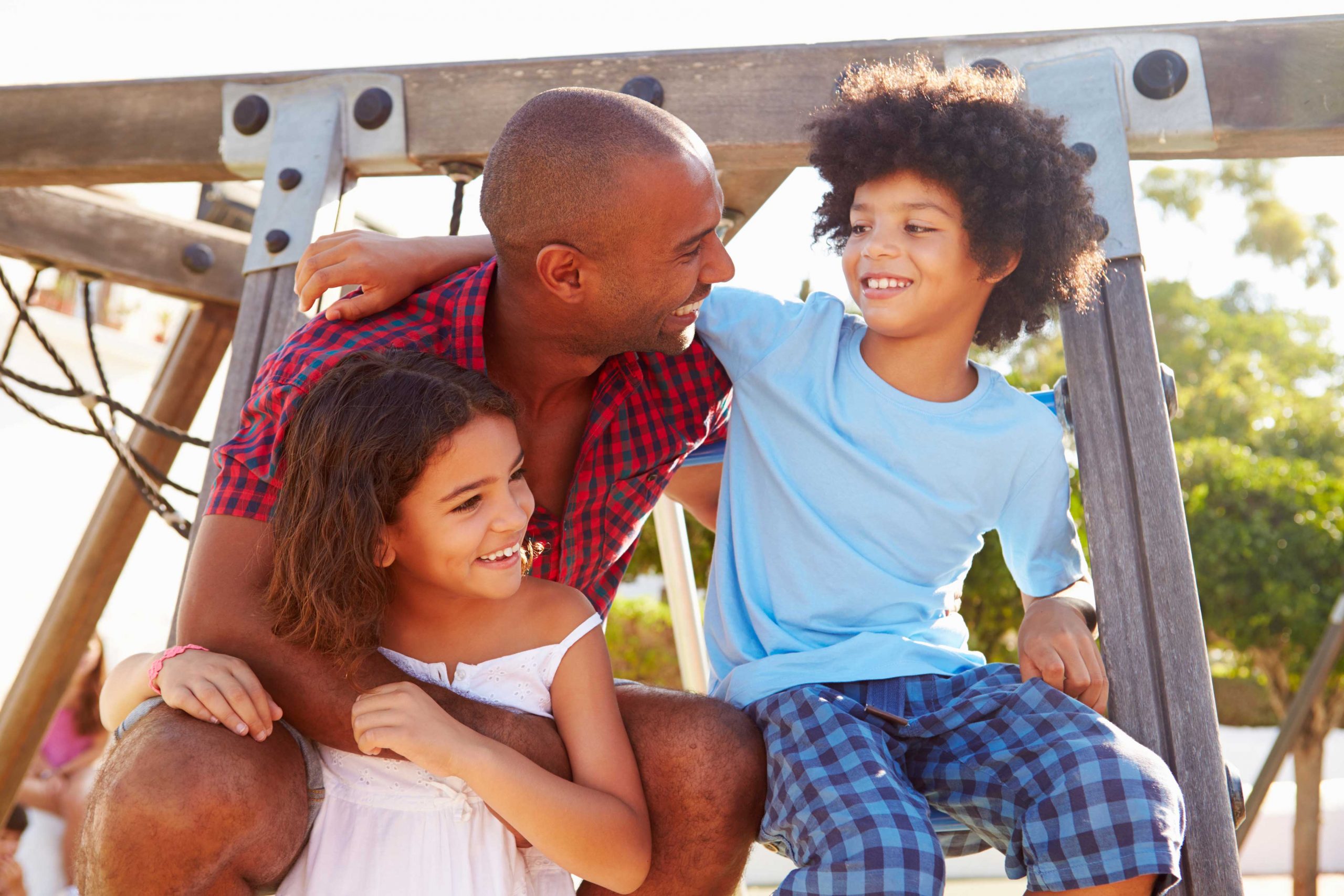 A father holds his daughter and son on a playground set