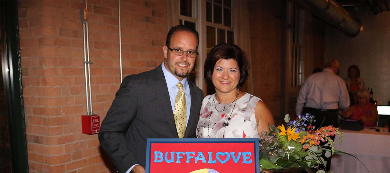 A nicely dressed man and woman smile while holding a sign saying "Buffalove"