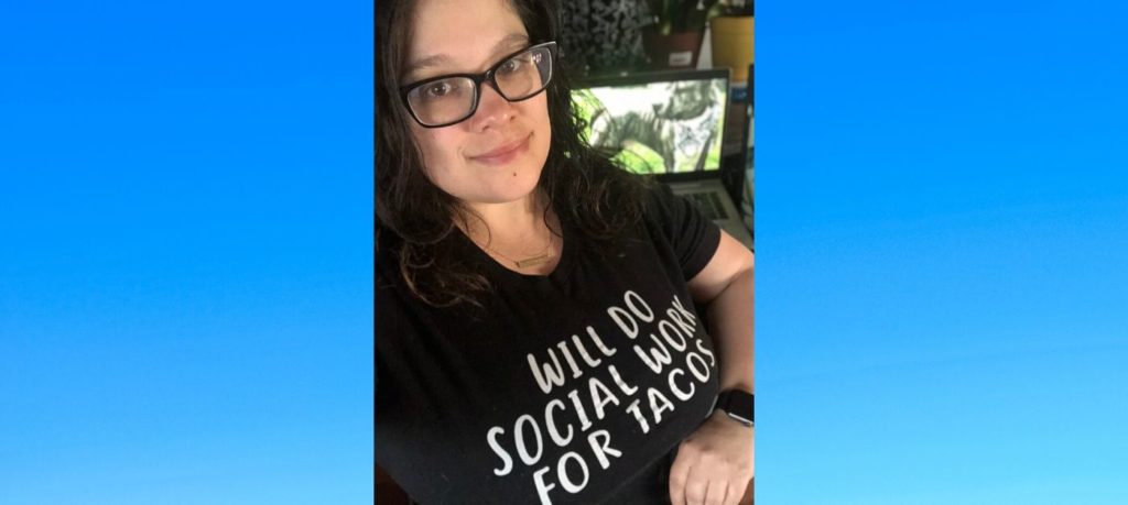 Selfie of a woman wearing glasses and a black shirt that says "Will Do Social Work for Tacos"