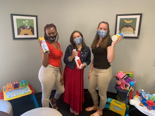 Three women wearing masks hold cleaning supplies