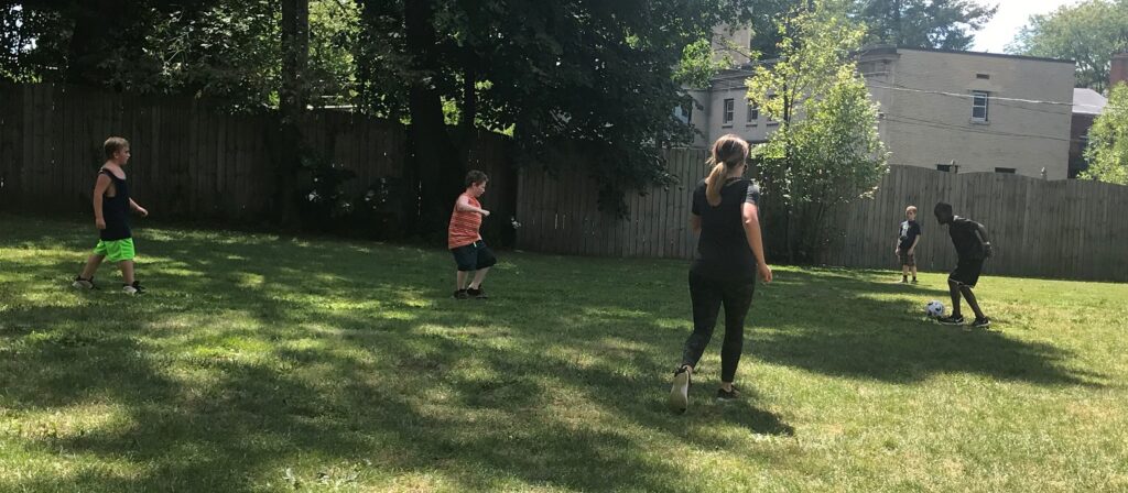 A group of children play soccer on a grass lawn