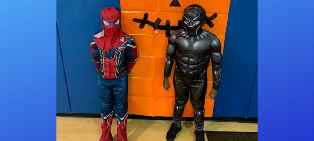 Children dressed as Spider-Man and Black Panther stand in front of a Pumpkin decoration on a wall