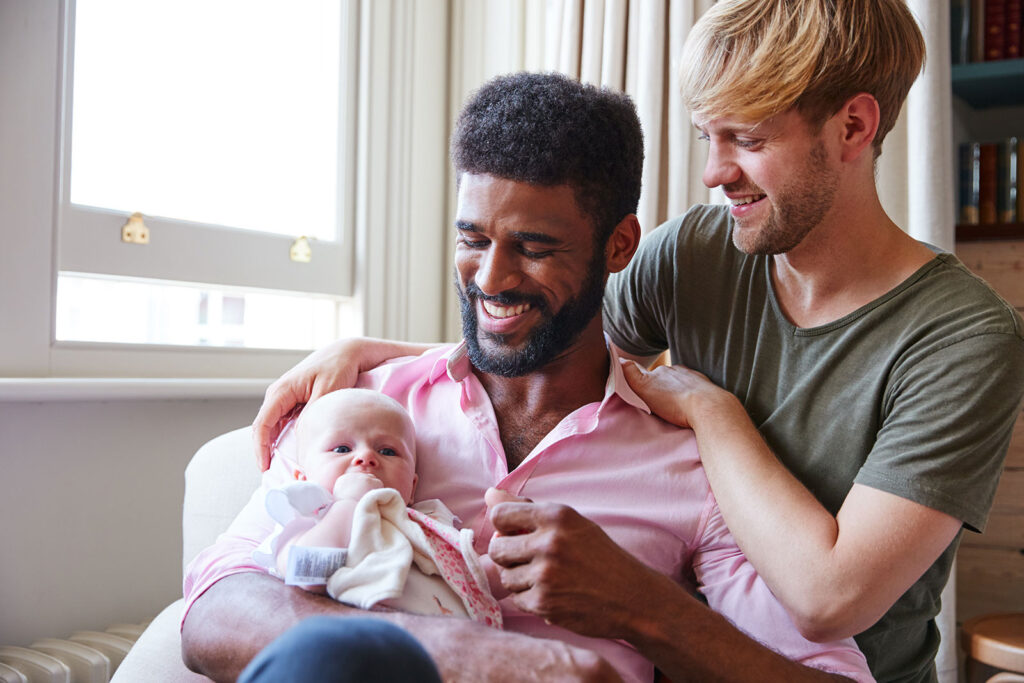 Loving same-sex male couple cuddle baby daughter on couch