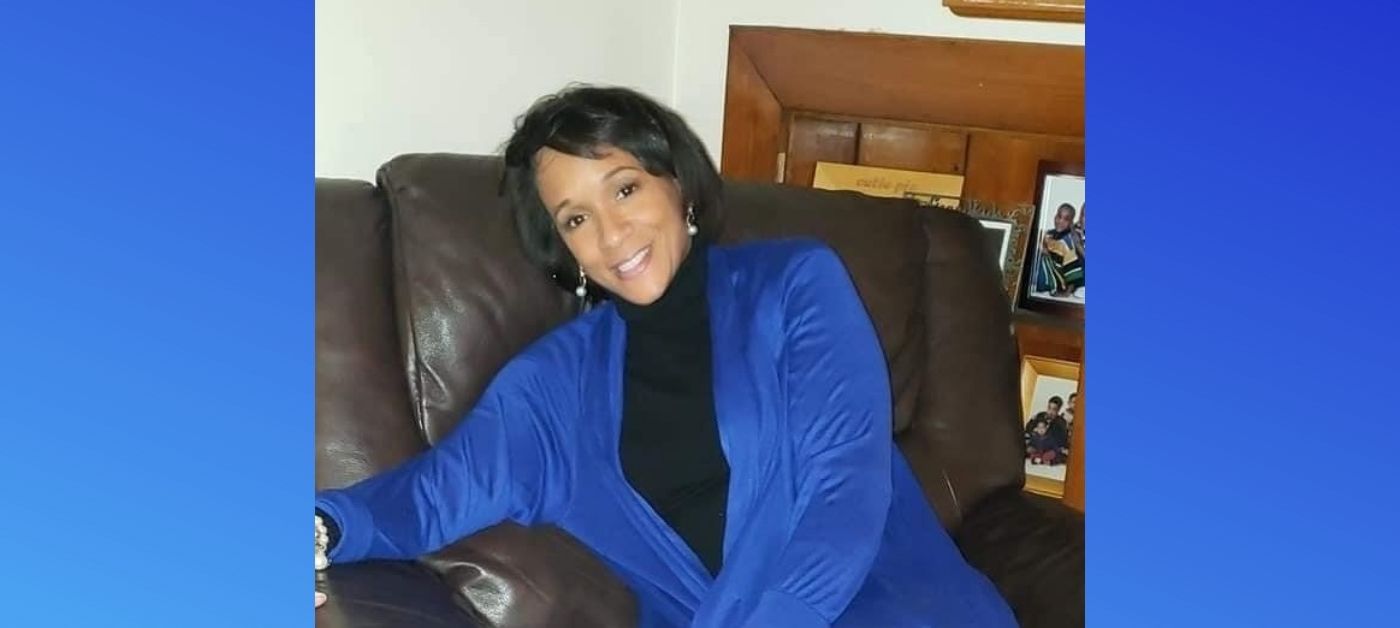 A woman in a blue jacket and black shirt smiles on a brown lounge chair