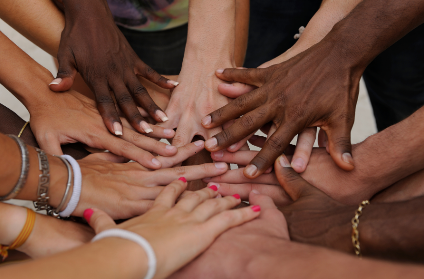 Hands of various skin colors pile together in a circle