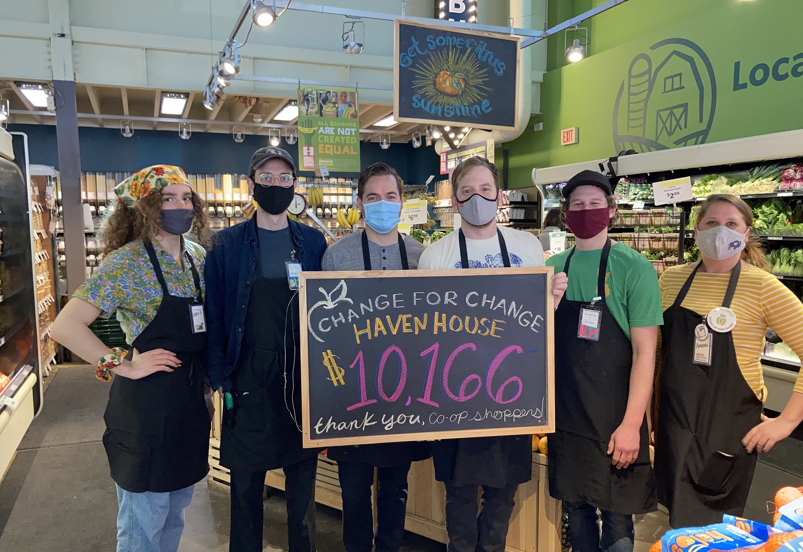 Six workers stand in a grocery store holding a blackboard with "$10,166" written on it in pink