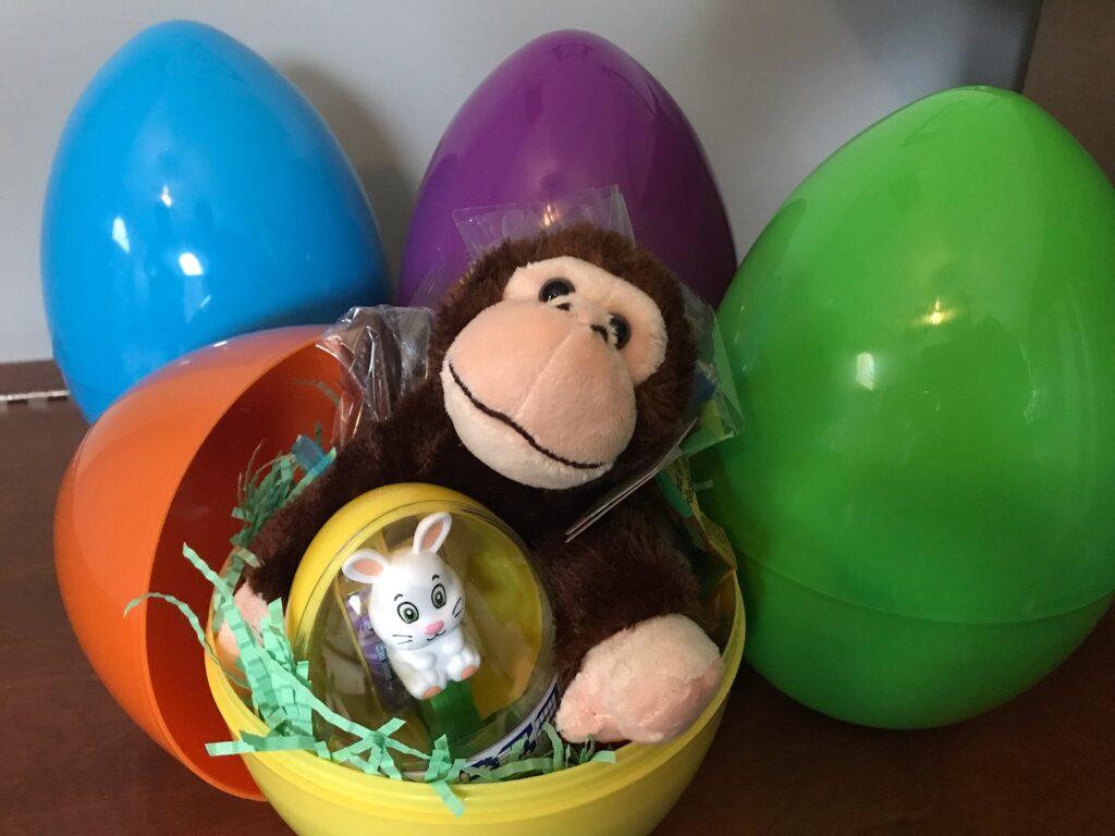 A stuffed monkey sits in a yellow Easter egg surrounded by other colorful eggs