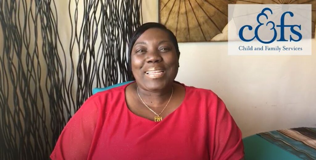 A woman in a red shirt smiles directly at the camera