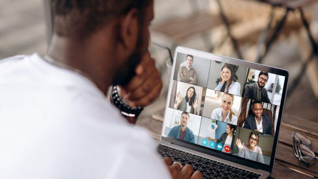 A man looks at his laptop, which shows a Zoom meeting with nine other users filling the screen