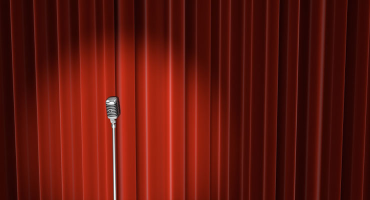 A microphone sits in front of a red curtain, highlighted by a spotlight