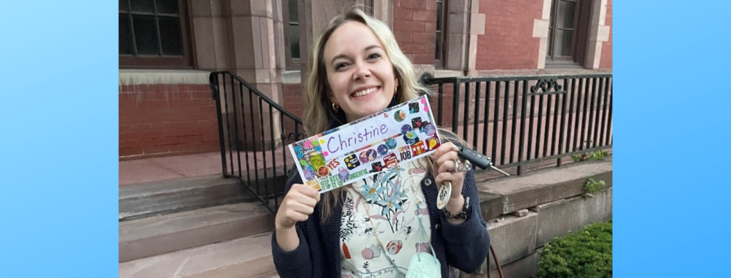 A smiling woman holds up a nametag with her name on it. The nametag is covered in stickers.